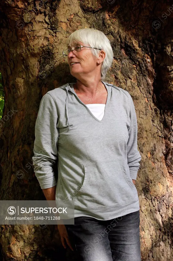 Elderly woman, senior citizen, leaning against a tree