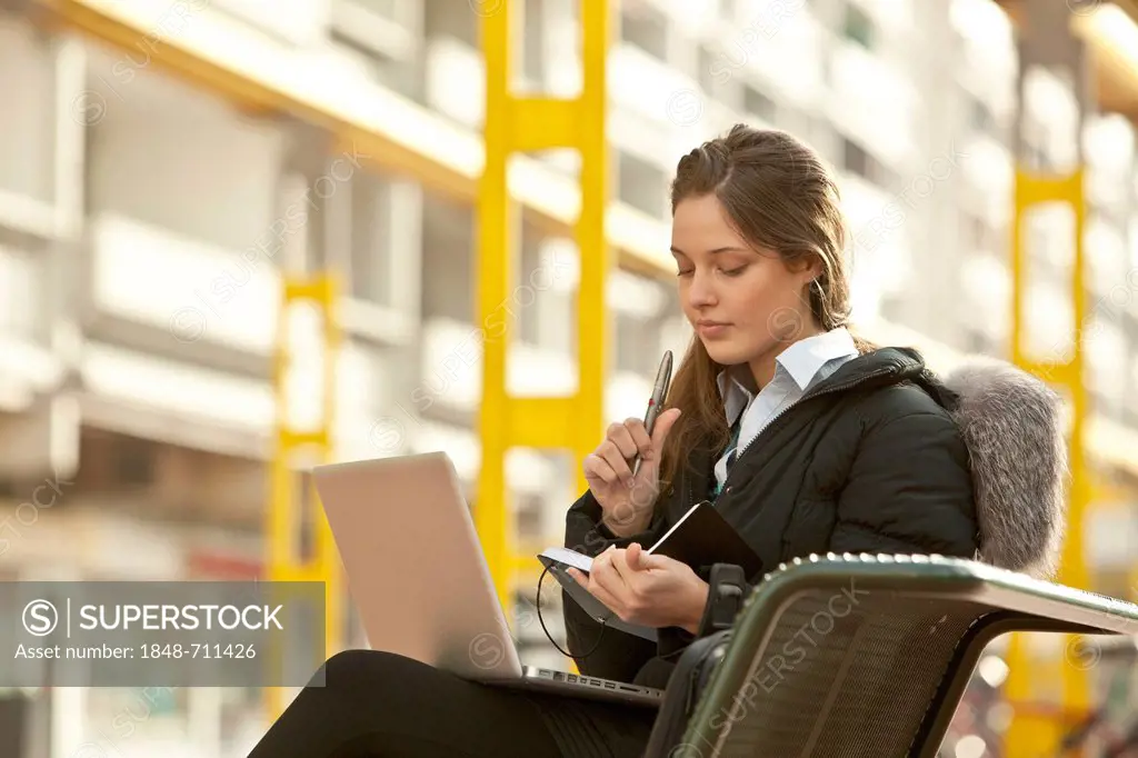 Student with a laptop and a notebook sitting on a bench