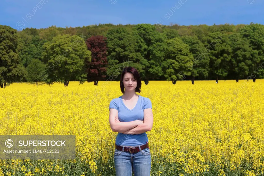 Young woman with her eyes closed and her arms crossed standing in front of a field of rape, Swabian Alb, Baden-Wuerttemberg, Germany, Europe