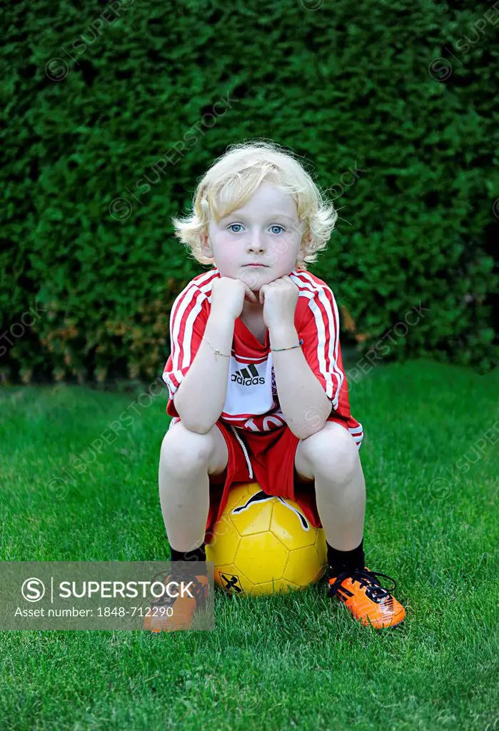 Five-year-old boy wearing a FC Bayern Munich soccer dress, sitting on a yellow soccer ball