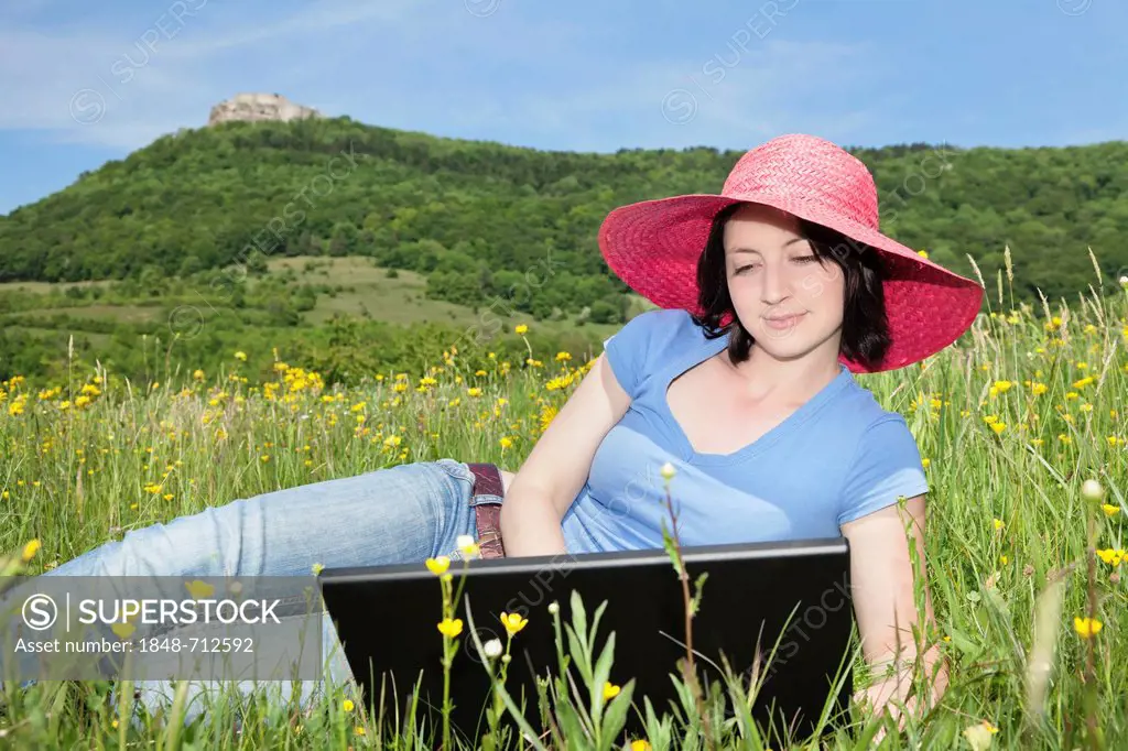 Young woman wearing a red hat using a laptop in a meadow