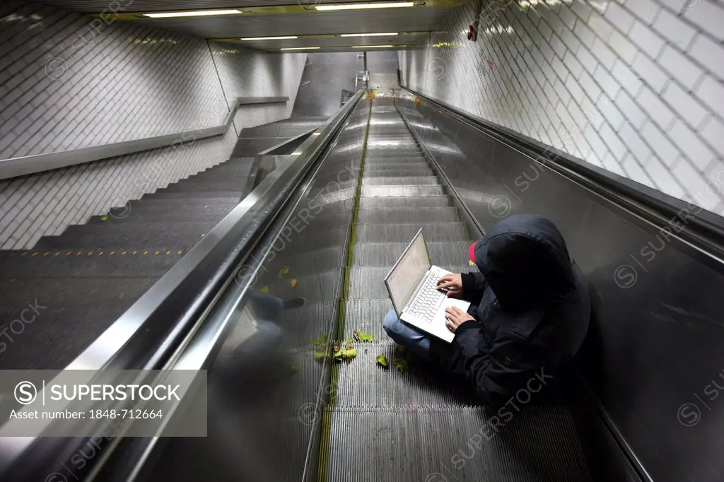Hacker surfing on a laptop computer on an escalator in a subway passage, symbolic image for computer hacking, computer crime, cybercrime, data theft