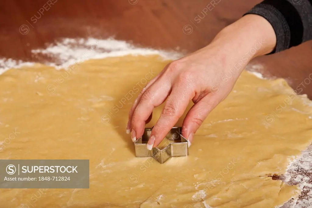 Woman's hand using a cookie cutter to cut Christmas cookies out of the dough