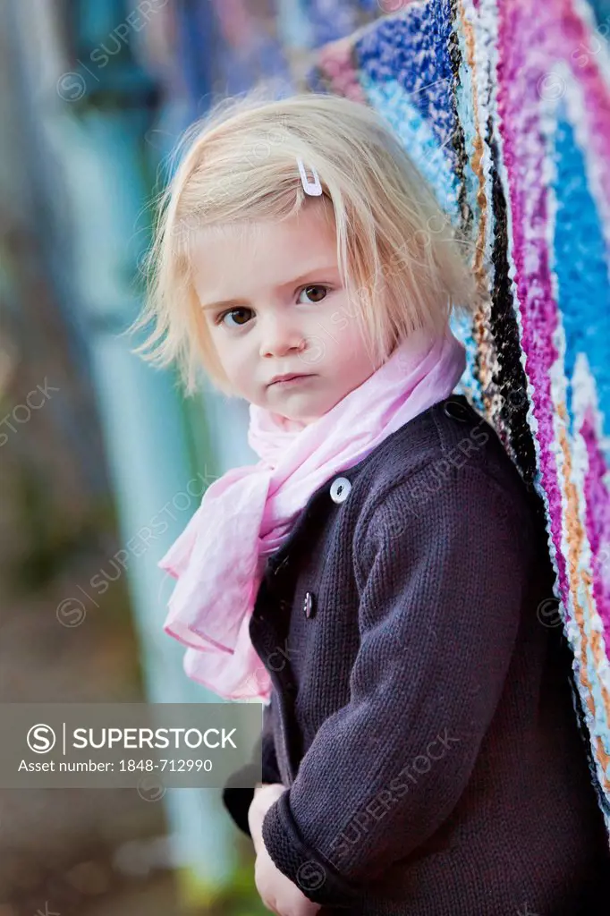 Girl, two years, leaning against a wall with graffiti