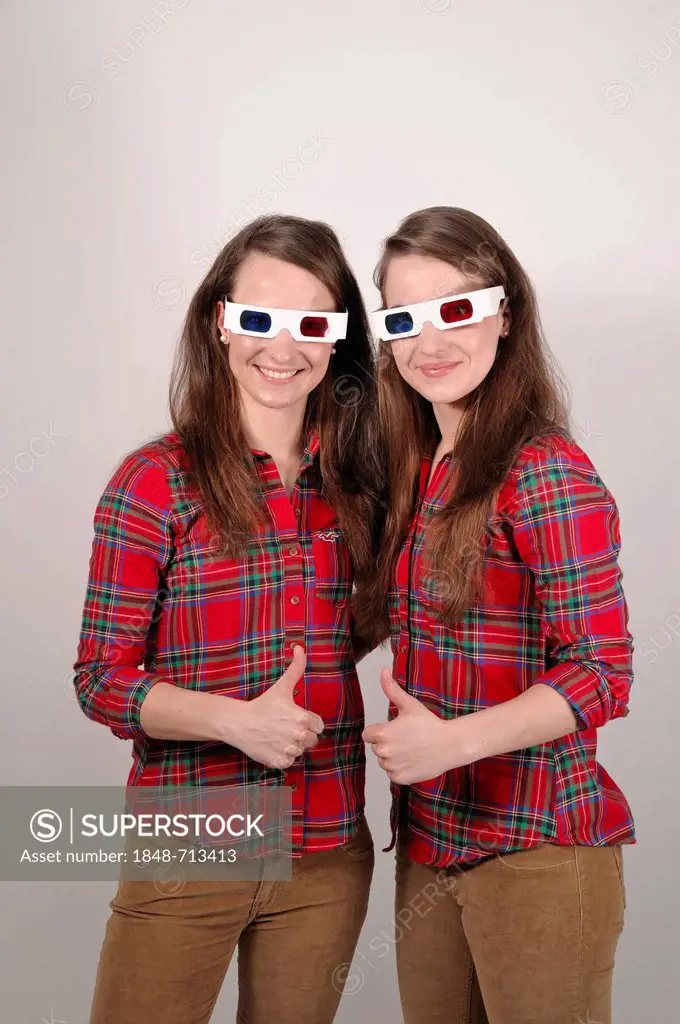 Twin sisters wearing 3D glasses holding up their thumbs