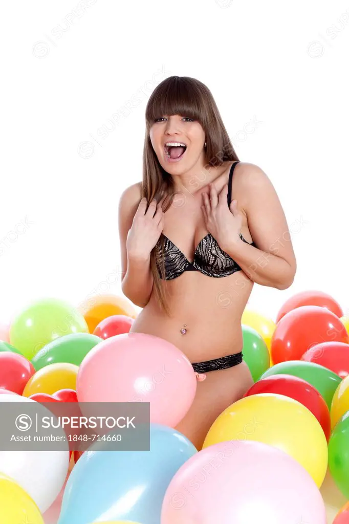 Young woman wearing lingerie sitting between colourful balloons and screaming with joy