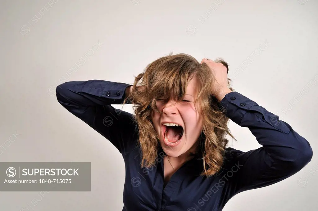 Young woman, 20, angry, screaming, holds her hands to her head and tearing at her hair