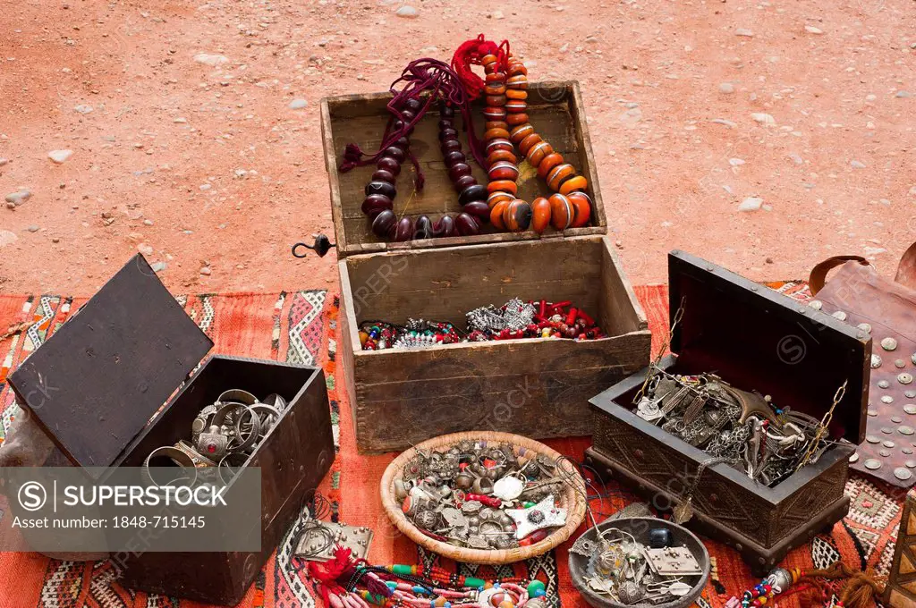 Oriental jewellery, small treasure chests, necklaces, rings, bracelets and decorated pendents are spread on a carpet in a souk or bazaar, Morocco, Afr...