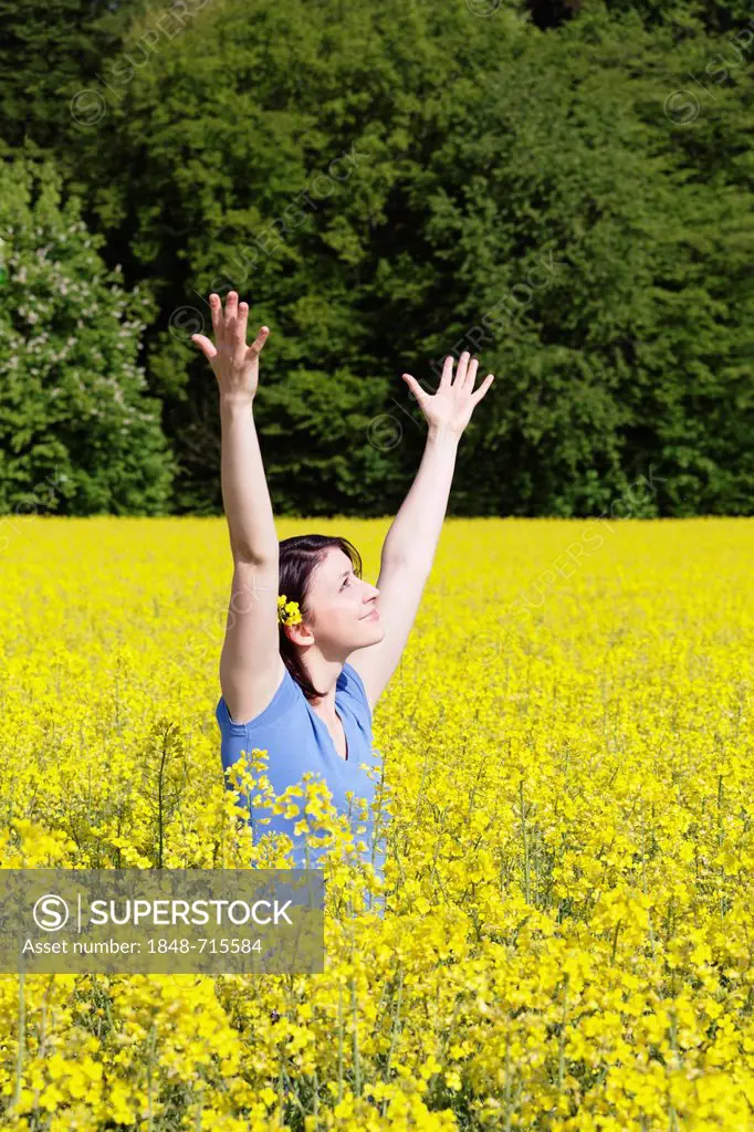 Young woman standing in a field of rape with rape flowers in her hair, full of vitality, Swabian Alb, Baden-Wuerttemberg, Germany, Europe