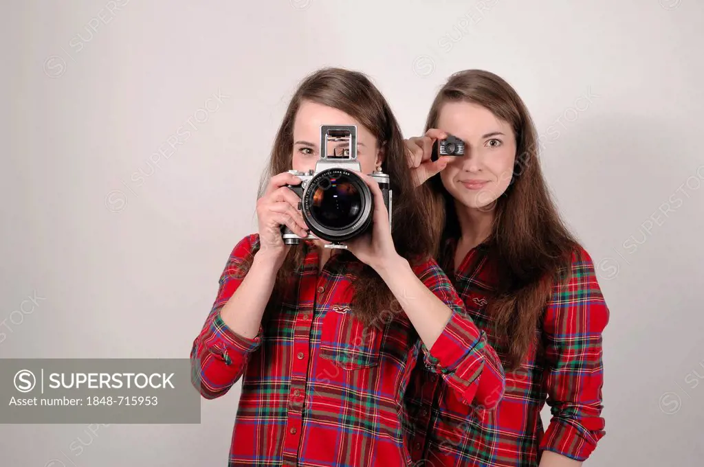 Twin sisters holding cameras, one holding a Pentacon Six medium format analogue camera, the other holding a mini-toy camera