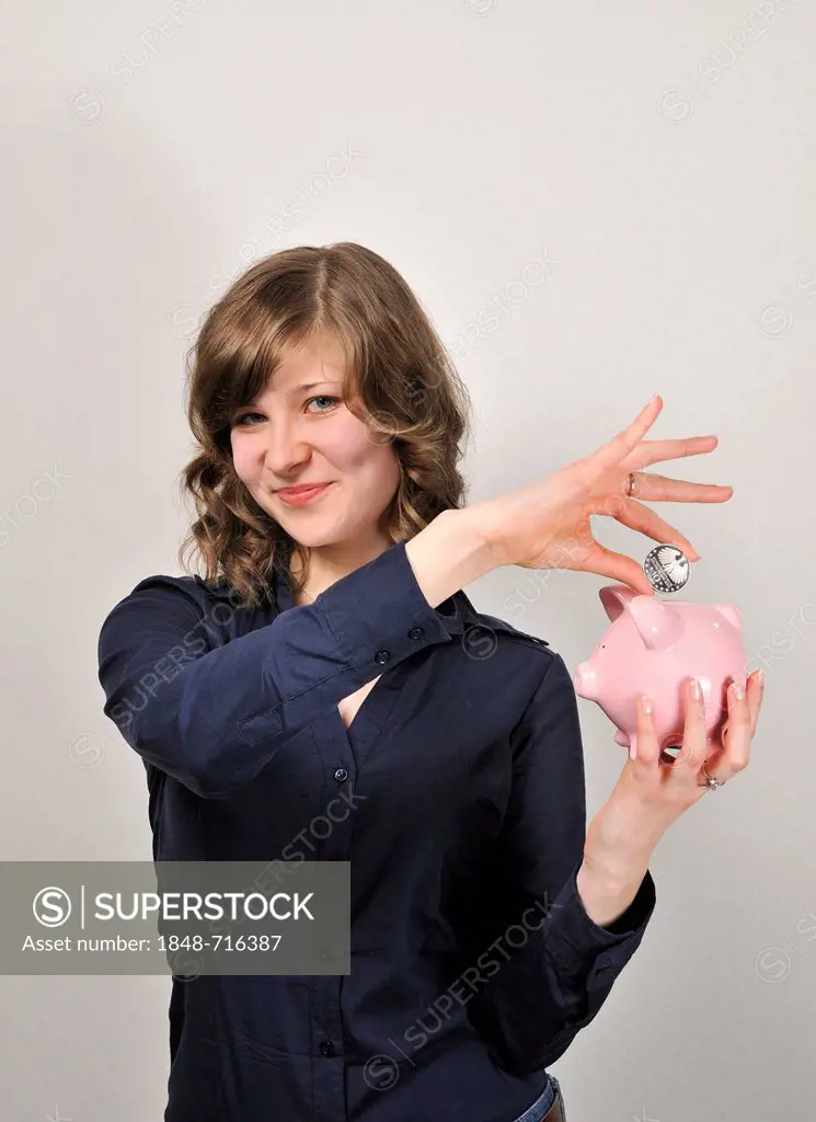 Young woman, 20, putting a 10 euro silver coin in a pink piggy bank