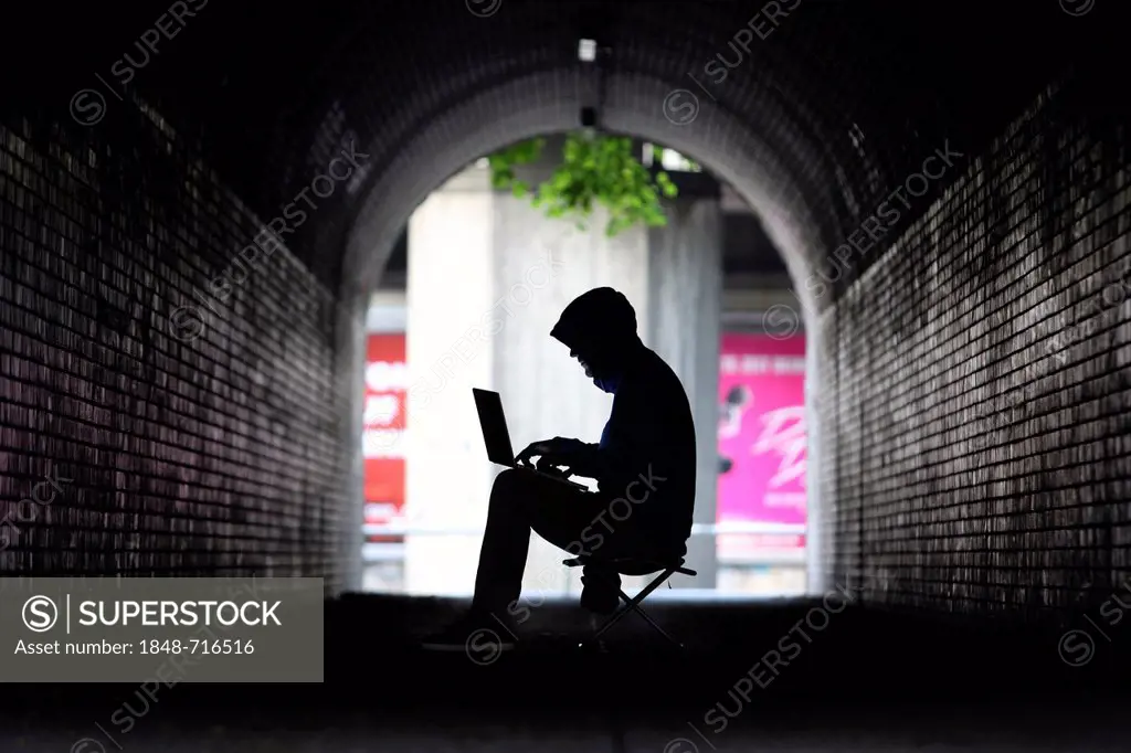Man surfing on a laptop computer in a pedestrian tunnel, symbolic image for computer hacking, computer crime, cybercrime, data theft