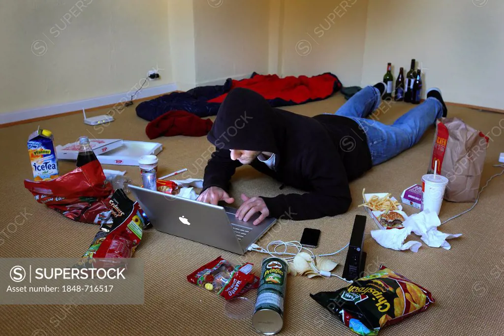 Hacker working on a laptop computer in a sparsely furnished apartment, symbolic image for computer hacking, computer crime, cybercrime, data theft