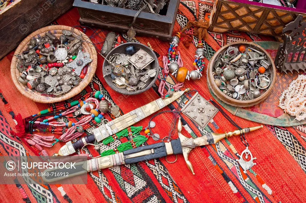 Oriental jewellery, small treasure chests and ornate Touareg knives are spread on a carpet in a souk or bazaar, Morocco, Africa