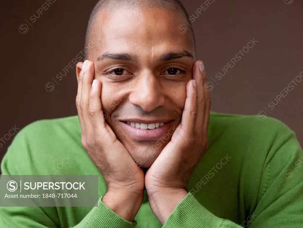 Smiling young man, dark-skinned, head resting on hands, portrait