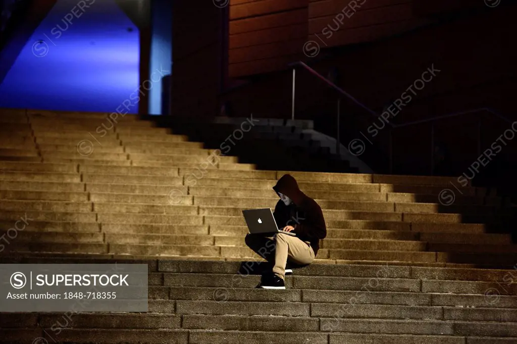 Man surfing on a laptop computer on a staircase at dusk, symbolic image for computer hacking, computer crime, cybercrime, data theft