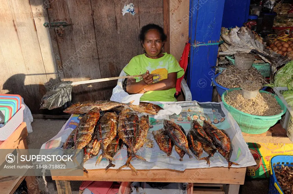 Papuan woman selling fried fish at the fish market in Kota Biak, waving the flies away with a plastic bag on a stick, Biak Island, West Papua, Indones...