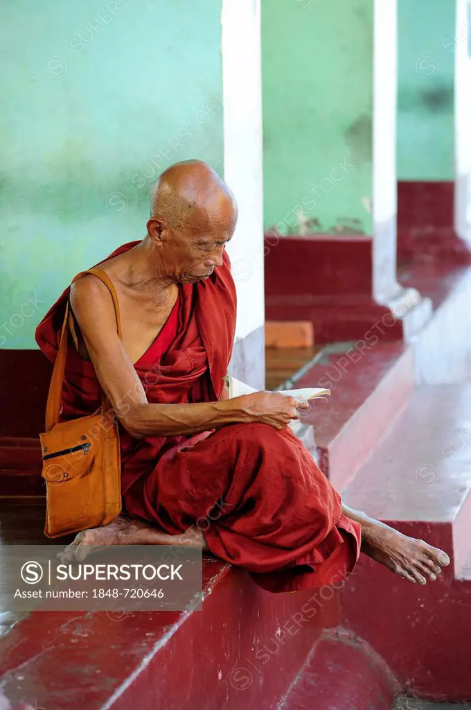 Reading monk sitting between the pillars of the Shwedagon Pagoda in Yangon, Myanmar, Burma, Southeast Asia, Asia