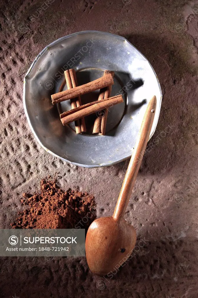 Cinnamon sticks (Cinnamomum) on a metal plate with a wooden spoon and cinnamon powder on a rustic stone base