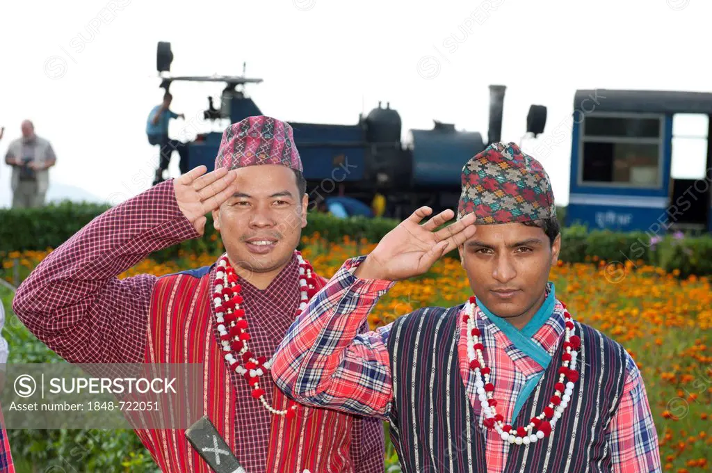 Two Nepali men in traditional costume saluting, historic train at back, Darjeeling Himalayan Railway, narrow-gauge railway, Toy Train, UNESCO World He...