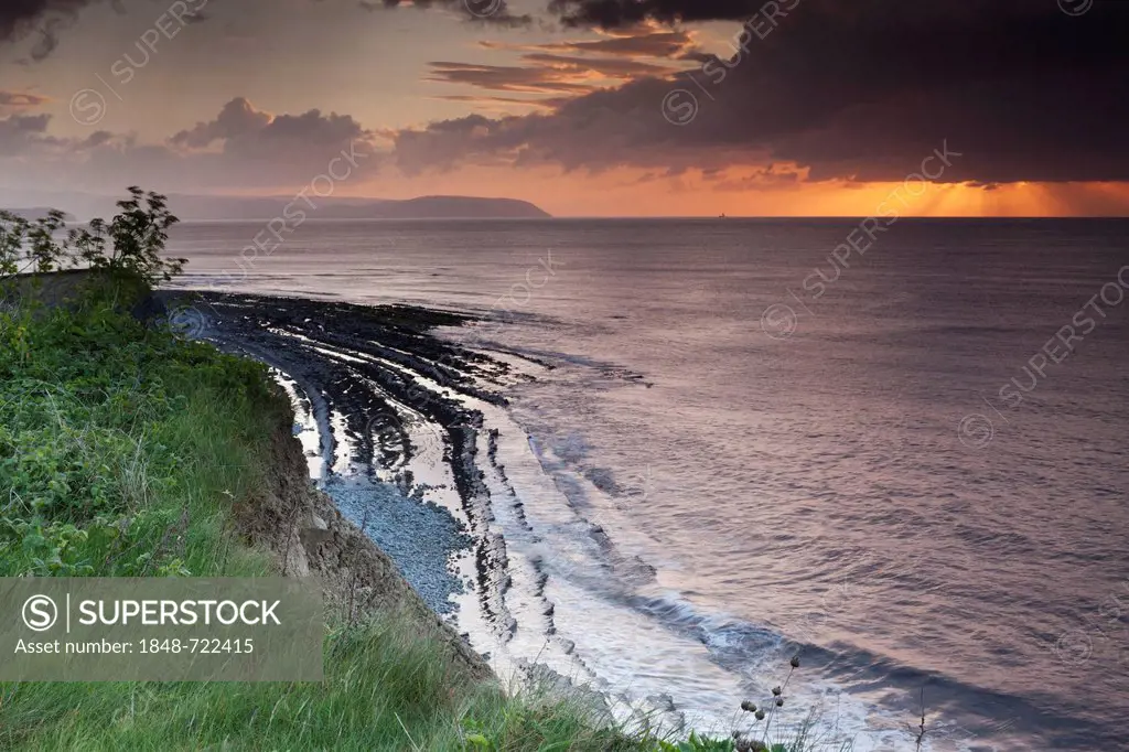 Setting sun shining through a heavy cloud with rays over the Bristol Channel, from the cliffs above Kilve Beach, Somerset, England, United Kingdom, Eu...