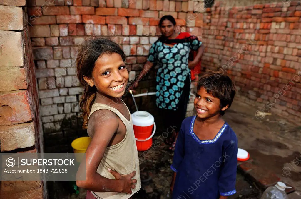 Woman and girls collecting water from a tap, they live and work with their family under the slavery-like practice of debt bondage in a brick factory, ...