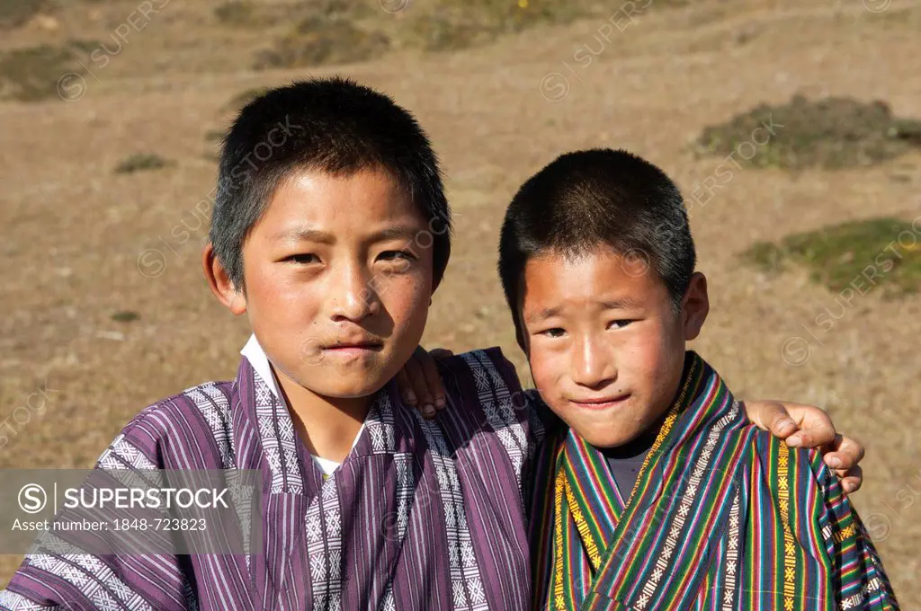 Two boys standing arm in arm on a pasture, traditional costume, Gho, near Gangtey Goenba, Gangteng Monastery, Phobjika Valley, the Himalayas, Bhutan, ...