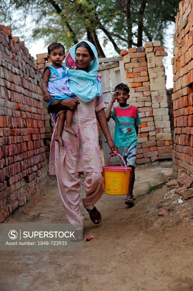 Woman carrying her daughter in her arms while fetching water, she lives and works with her family under the slavery-like practice of debt bondage in a...