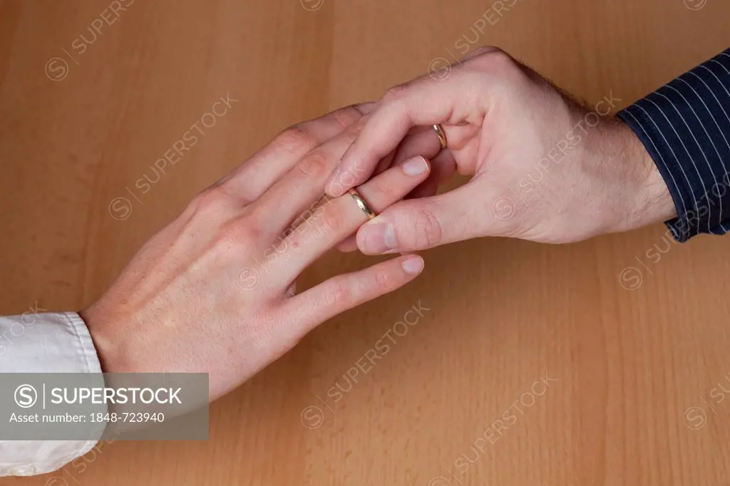 Hands of a young couple getting married, young man, 23, slipping a wedding ring on the hand of a young woman, 27