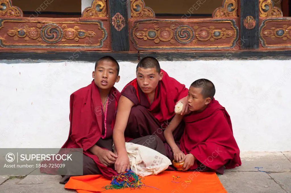 Tibetan Buddhism, three novices sitting on the ground wearing red robes, Rinpung Dzong Monastery and Fortress, courtyard, Paro, Himalayas, Bhutan, Sou...