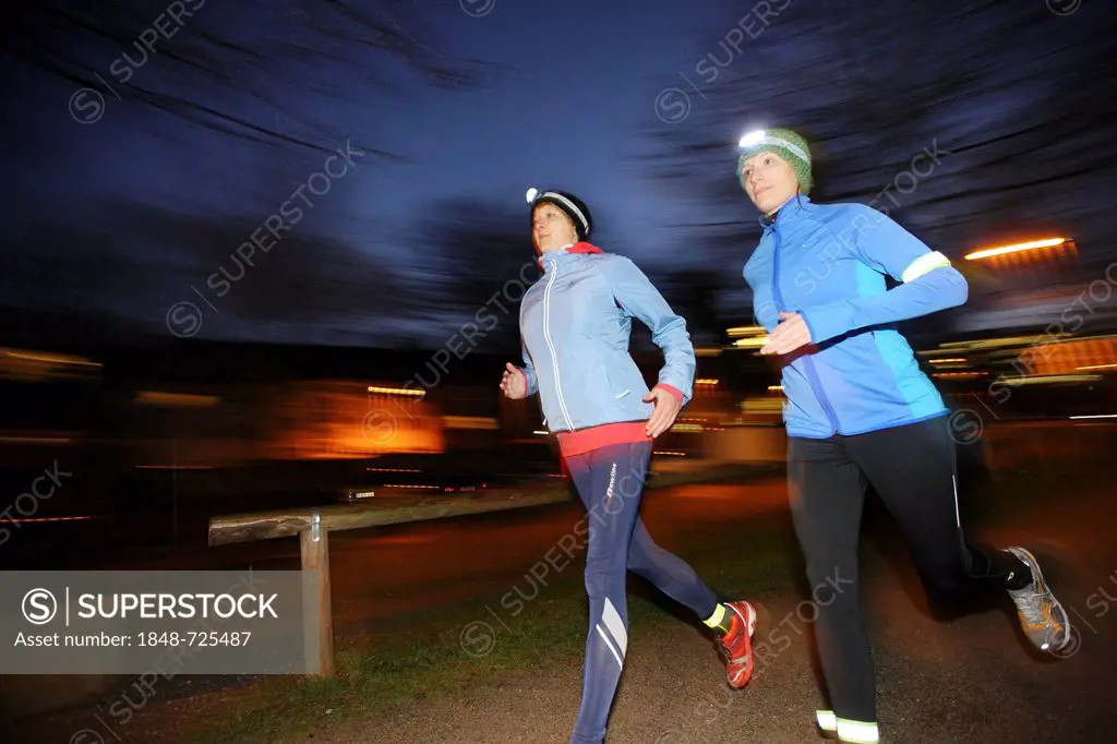 Two young women jogging at dusk in winter clothing with reflective strips, LED headlights and wind and waterproof functional clothing, Germany, Europe