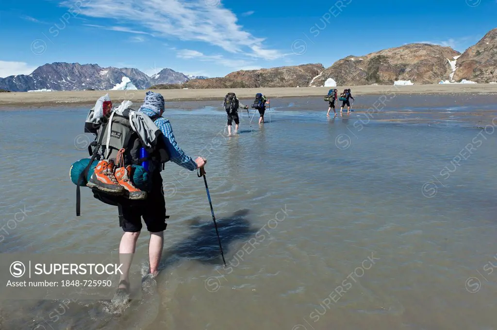 Group of hikers with backpacks crossing a creek at Sermelik Fjord, Ammassalik Peninsula, East Greenland, Greenland