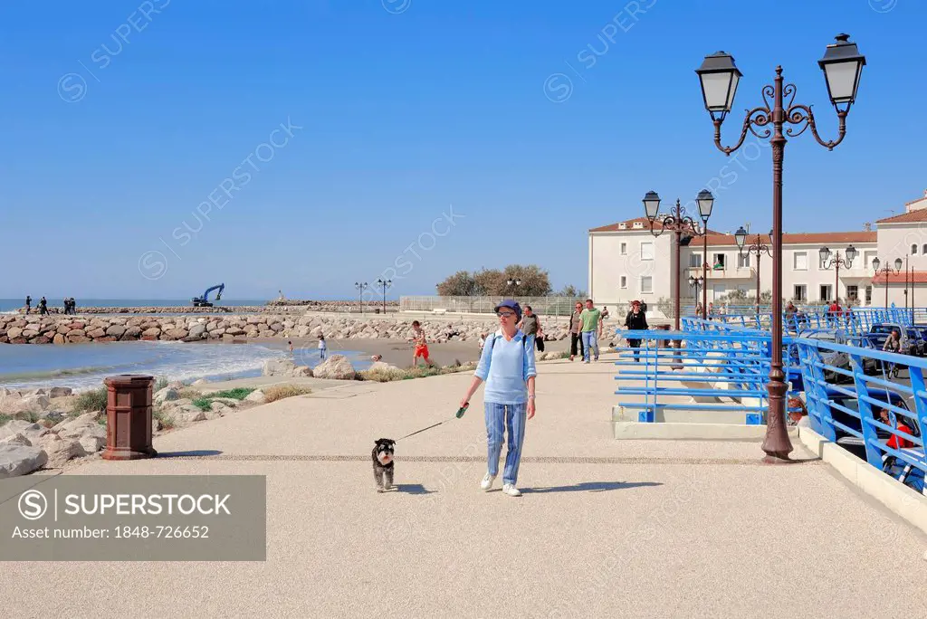 Woman with a miniature schnauzer walking on the beach promenade, Les Saintes-Maries-de-la-Mer, Camargue, Bouches-du-Rhone department, Provence-Alpes-C...