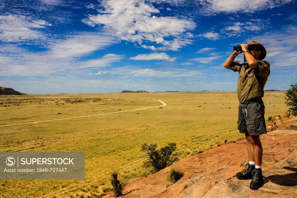 Man looking through binoculars into Damaraland, Namibia, Africa