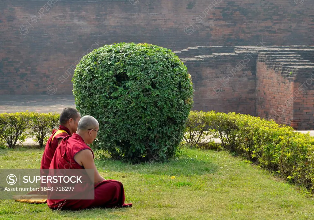 Tibetan Buddhist monks in red robes in meditation and prayer on a pilgrimage at the archaeological site of the ancient University of Nalanda, Global B...