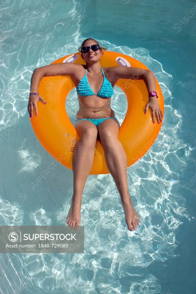 Young woman sitting on an inner tube, floating tyre, in a private swimming pool, Germany