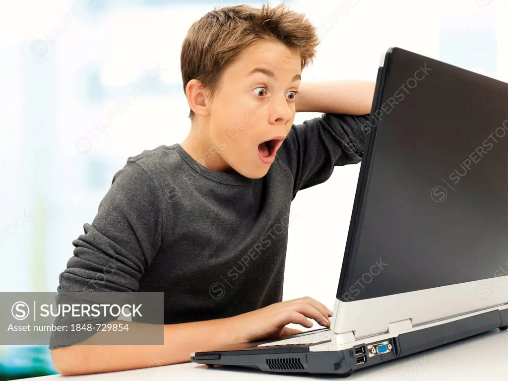Portrait, boy, teenager sitting in front of laptop, looking surprised