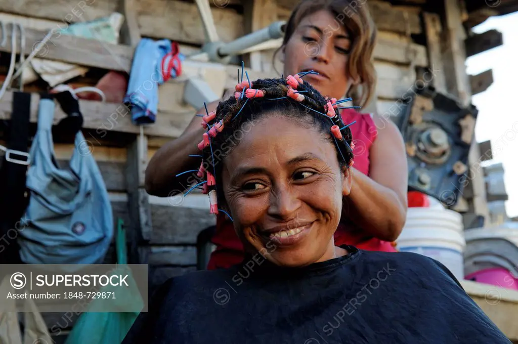 Woman doing another woman's hair in front of her hut, customer is 40 years old, in a poor neighborhood, Cancun, Yucatan Peninsula, Quintana Roo, Mexic...