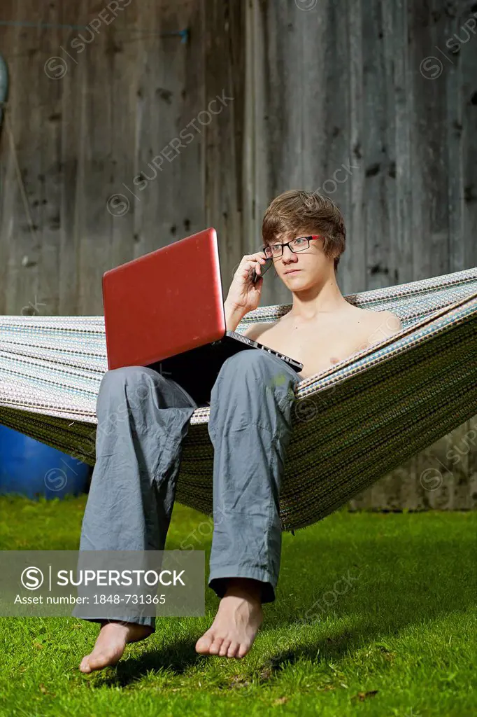 Teenager sitting in a hammock with a laptop speaking on his mobile phone