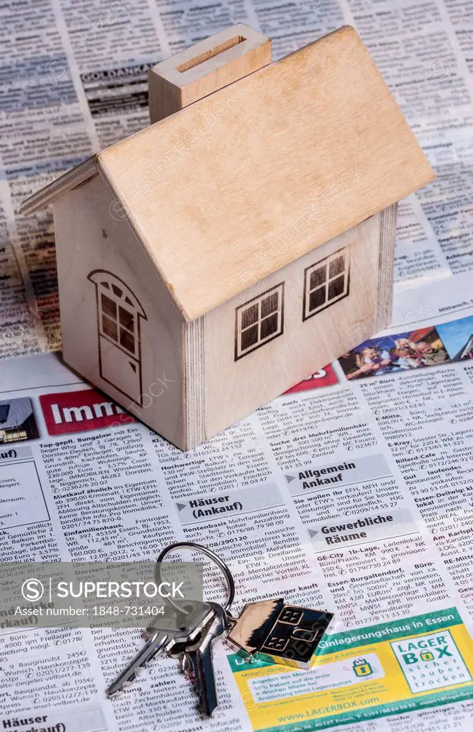 A little wooden house and two keys with a metal key tag shaped like a house, on the real estate page of a German daily newspaper, symbolic image for h...
