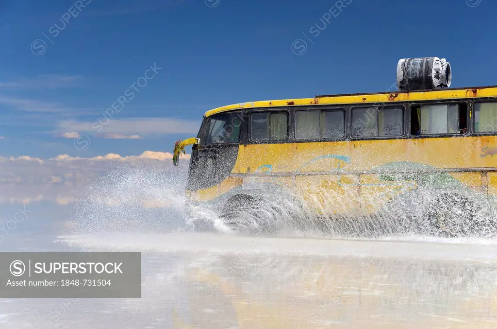 Yellow bus driving across the Salar de Uyuni, splashing water, Bolivia, South America