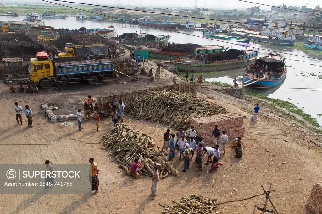 Firewood stored for sale on the shore, men circling the seller, carriers carrying coal from a barge to a truck at the rear, the Turag River, Gabtoli, ...