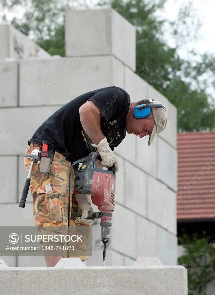 Construction worker drilling holes into concrete blocks during a building site load test at a construction site in Fridolfing, Bavaria, Germany, Europ...