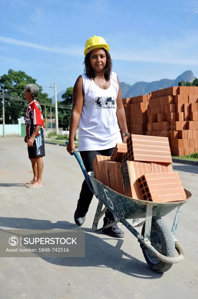 Woman from the slums, favelas, transporting bricks in a wheelbarrow on a building site of the Esperanca housing co-operative, each family helping out ...