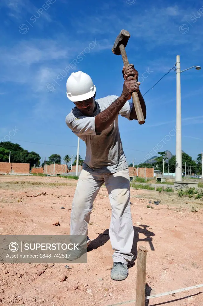 Man with a sledge hammer hitting a peg in the ground, people from the slums, favelas, working together on a building site of the Esperanca housing co-...