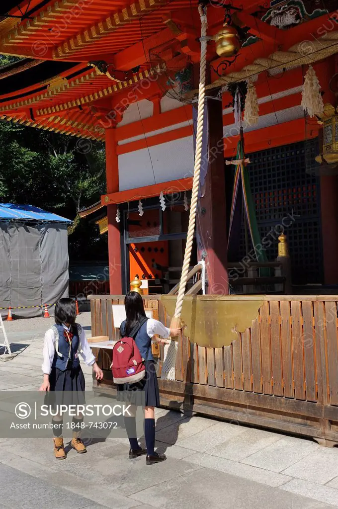 Students wearing school uniforms ringing the bell on a shrine to draw the spirits' attention to them, Yasaka Shrine, Maruyama Park, Kyoto, Japan, East...
