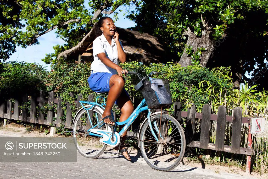 Woman talking on a mobile phone while riding a bicycle, La Digue Island, Seychelles, Africa, Indian Ocean