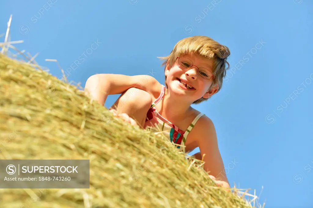 Girl, six years, with glasses and gaps in teeth, on a straw bale, Germany, Europe