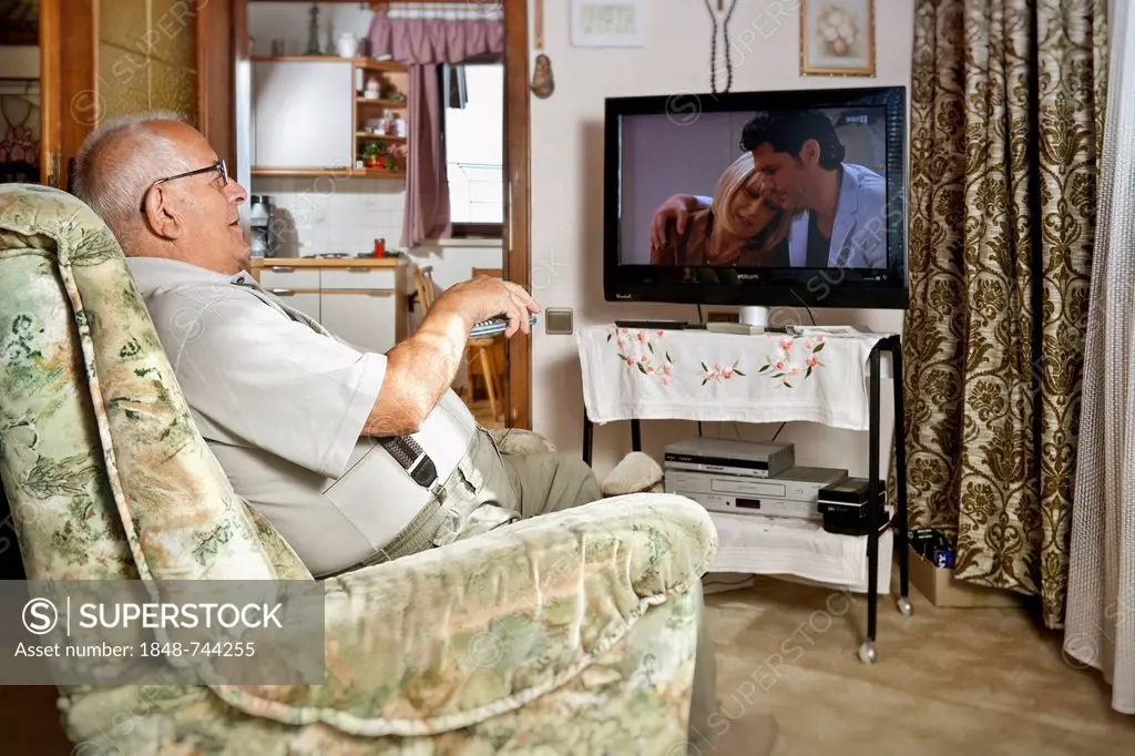Elderly man sitting in front of a TV operating a remote control