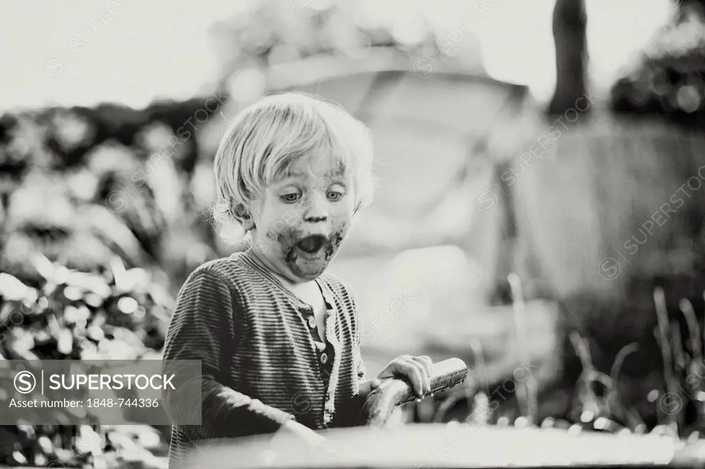 Young boy with his mouth smeared with chocolate looking shocked at a wheelbarrow